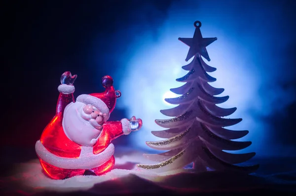 Boneca Feliz Papai Noel na época de Natal com árvore e neve. Fundo bokeh colorido. Papai Noel e Feliz Natal modelo figura brinquedo no fundo enevoado tonificado escuro . — Fotografia de Stock