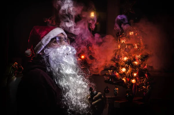 Kerstman vaping elektronische sigaret verkleed als traditionele Santa op een donker getinte achtergrond met vape wolken. Selectieve aandacht — Stockfoto