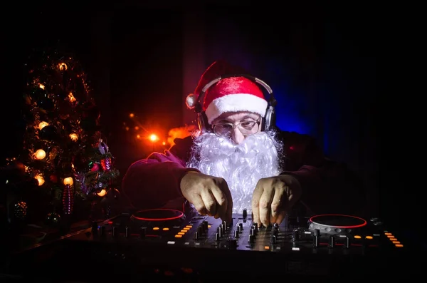 DJ Papai Noel misturando um pouco de alegria de Natal. Clube de discoteca escuro tonificado fundo. Evento de Ano Novo nos raios de luz. Útil como cartaz. Foco seletivo — Fotografia de Stock