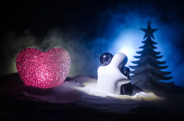 爱新年的概念 女孩和男孩陶瓷的数字拥抱对方 站在白色的雪和彩色的心和圣诞树上模糊的黑暗背景 空的空间 拥抱雕塑 — 图库照片
