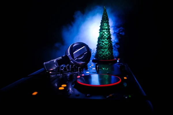 Dj mixer with headphones on dark nightclub background with Christmas tree New Year Eve. Close up view of New Year elements or symbols (Santa Clause, Snowman, Dog 2018, gift box) on a Dj table.