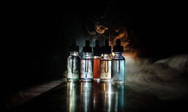 Vape concept. Smoke clouds and vape liquid bottles on dark background. Light effects. Useful as background or vape advertisement or vape background.
