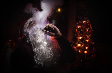 Santa Clause vaping electronic cigarette dressed as traditional Santa on a dark toned background with vape clouds. Selective focus clipart
