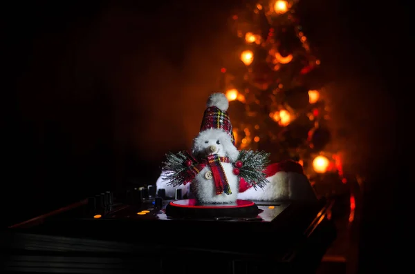 Dj mixer with headphones on dark nightclub background with Christmas tree New Year Eve. Close up view of New Year elements or symbols (Santa Clause, Snowman, Dog 2018, gift box) on a Dj table. toned