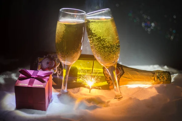 Capodanno sfondo celebrazione con coppia di flauti e bottiglia di champagne con attributi di Natale (o elementi) su sfondo nebbioso scuro nevoso tonica. Focus selettivo . — Foto Stock