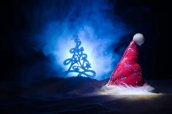 Νέο έτος διακοπών Χριστούγεννα φόντο με καπέλο Santa Clause και θολή χριστουγεννιάτικο δέντρο σε χιονισμένο φόντο. Νέο έτος εννοιολογική εικόνα διακόσμηση με χαρακτηριστικά διακοπών. Σκούρο φόντο Toned — Φωτογραφία Αρχείου