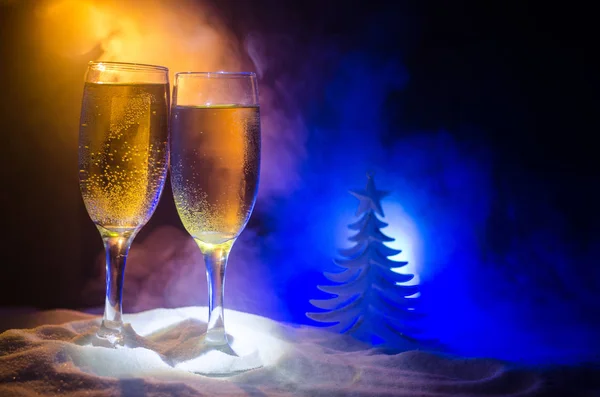 Capodanno sfondo celebrazione con coppia di flauti e bottiglia di champagne con attributi di Natale (o elementi) su sfondo nebbioso scuro nevoso tonica. Focus selettivo . — Foto Stock