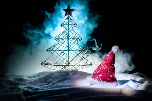 Christmas holiday New Year background with Santa Clause hat and blurred Christmas tree on snowy background. New Year conceptual image decoration with holiday attributes. Dark Toned background