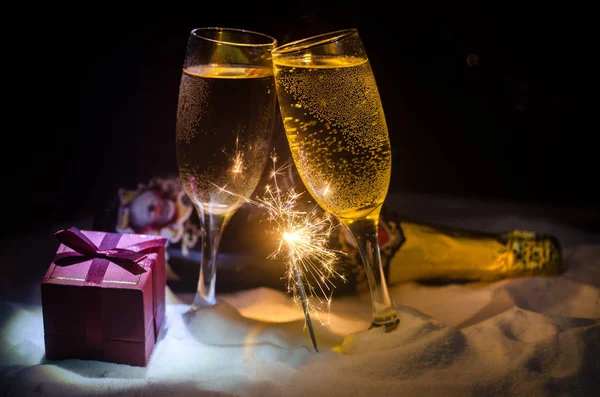 Capodanno sfondo celebrazione con coppia di flauti e bottiglia di champagne con attributi di Natale (o elementi) su sfondo nebbioso scuro nevoso tonica. Focus selettivo . — Foto Stock