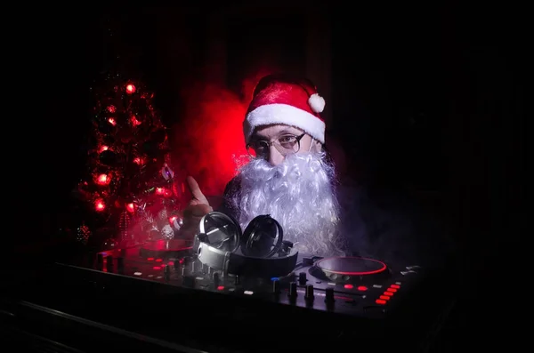 DJ Santa Claus mixing up some Christmas cheer. Dark disco club toned background. New Year's Eve event in the rays of light. Useful as poster. Selective focus — Stock Photo, Image