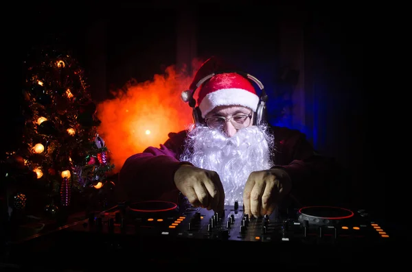 Mikołaj DJ mieszanie się niektóre dopingować Boże Narodzenie. Ciemny dyskoteka stonowanych tła. New Year's Eve zdarzenia w promienie światła. Użyteczne jako plakat. Selektywny fokus — Zdjęcie stockowe