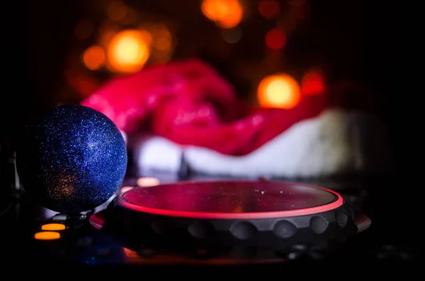 Dj mixer with headphones on dark nightclub background with Christmas tree New Year Eve. Close up view of New Year elements or symbols (Santa Clause, Snowman, Dog 2018, gift box) on a Dj table. toned