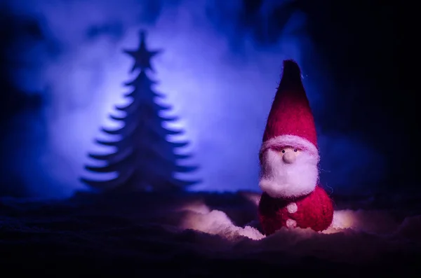 圣诞快乐圣诞老人娃娃在圣诞树和雪的时间。丰富多彩的散背景。圣诞老人和圣诞快乐模型图玩具在黑暗的色调 — 图库照片