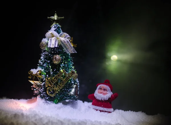 Happy Santa Claus Doll op Kersttijd met boom en sneeuw. Kleurrijke bokeh achtergrond. Kerstman en Merry Christmas model figuur speelgoed op donker getinte — Stockfoto