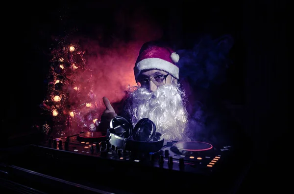 DJ Santa Claus mixing up some Christmas cheer. Dark disco club toned background. New Year's Eve event in the rays of light. Useful as poster. Selective focus — Stock Photo, Image