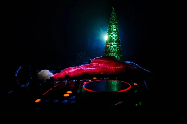 Dj mixer with headphones on dark nightclub background with Christmas tree New Year Eve. Close up view of New Year elements or symbols (Santa Clause, Snowman, Dog 2018, gift box) on a Dj table.