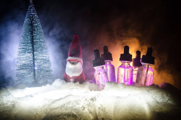 Electronic cigarette with vape liquids and christmas decorations on bokeh lights background with New Year atributes or symbols. Selective focus