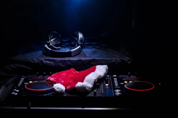 Dj mixer with headphones on dark nightclub background with Christmas tree New Year Eve. Close up view of New Year elements or symbols (Santa Clause, Snowman, Dog 2018, gift box) on a Dj table.