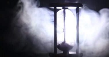 Zaman kavramı. Koyu tonlu arka plan veya semboller altında duman, son zamanların duman dönme kum saati saat silüeti