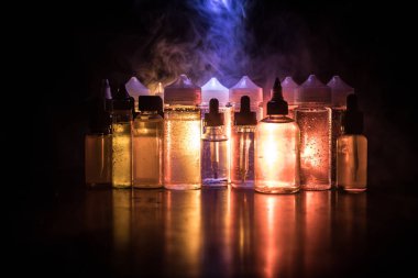 Vape kavramı. Duman bulutları ve vape sıvı şişe koyu arka plan üzerinde. Işık efektleri