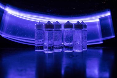Vape kavramı. Duman bulutları ve vape sıvı şişe koyu arka plan üzerinde. Işık efektleri
