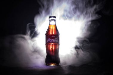Baku, Azerbaijan 13th January 2018, Coca-Cola Classic in a glass bottle on dark toned foggy Background. Coca Cola is the most popular carbonated soft drink beverages sold around the world clipart