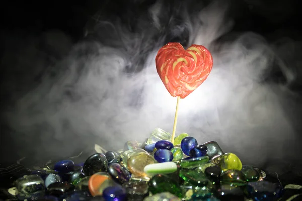Peu de sucettes de coeur de bonbons colorés sur différents bonbons colorés sur fond brumeux foncé . — Photo
