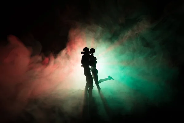 Love Valentine 's Day concept.Sillhouette of sweet young couple in love standing in the field and hugging on dark toned foggy background. Украшение с фигурками кукол на столе . — стоковое фото