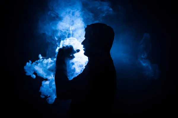 Hombre aspirante sosteniendo un mod. Una nube de vapor. Fondo negro. Vapeando un cigarrillo electrónico con mucho humo. Concepto de Vape — Foto de Stock