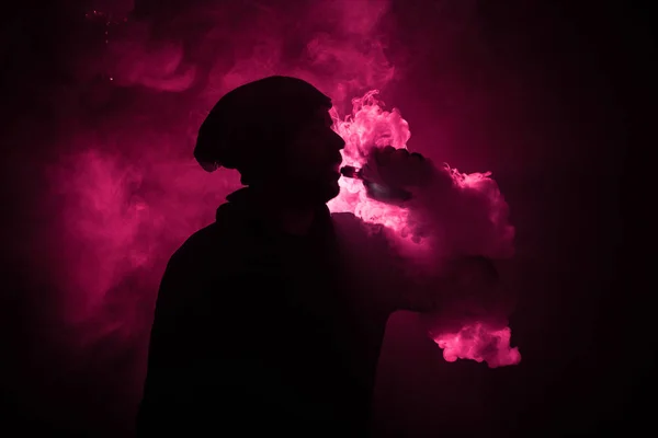 Vaping 男子手持一个 mod。蒸气云。黑色的背景。吸电子烟的大量黑烟与雾。Vape 概念 — 图库照片
