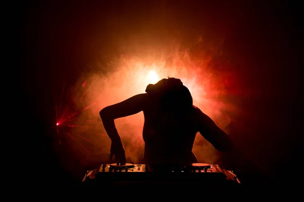 DJ Spinning, Mixing, and Scratching in a Night Club, Hands of dj tweak various track controls on dj\'s deck, strobe lights and fog, or Dj mixes the track in the nightclub at party