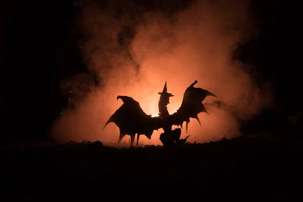 Silueta de fuego respirando dragón con grandes alas sobre un fondo naranja oscuro —  Fotos de Stock