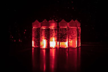 Vape kavramı. Duman bulutları ve vape sıvı şişe koyu arka plan üzerinde. Işık efektleri