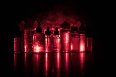 Vape kavramı. Duman bulutları ve vape sıvı şişe koyu arka plan üzerinde. Işık efektleri