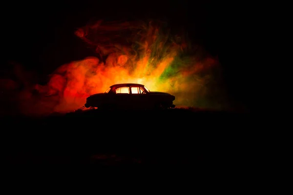 Silhouet van oude oldtimers in mistige donker getinte achtergrond met gloeiende lichten in weinig licht, of silhouet van oude misdaad auto donkere achtergrond. — Stockfoto
