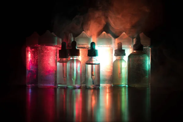 Vape concept. Roken wolken en vape vloeibare flessen op donkere achtergrond. Licht effecten — Stockfoto