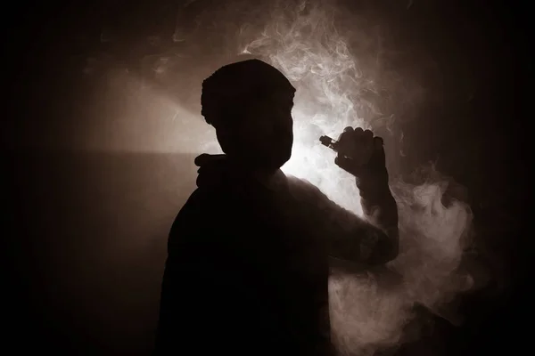 Un voleur tenant un mod. Un nuage de vapeur. Fond noir. Vaping une cigarette électronique avec beaucoup de fumée. Concept de forme — Photo