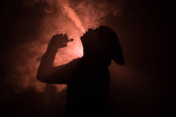 Vaping man holding a mod. A cloud of vapor. Black background. Vaping an electronic cigarette with a lot of smoke. Vape concept