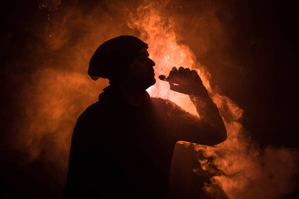 Vaping man holding a mod. A cloud of vapor. Black background. Vaping an electronic cigarette with a lot of smoke. Vape concept