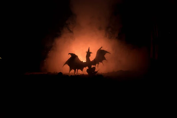 Silueta oheň chrlícího draka s velkými křídly na tmavě oranžové pozadí — Stock fotografie