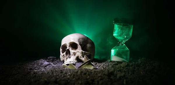Cráneo y reloj de arena vintage sobre fondo nebuloso tonificado oscuro bajo haz de luz. Concepto de horror . —  Fotos de Stock