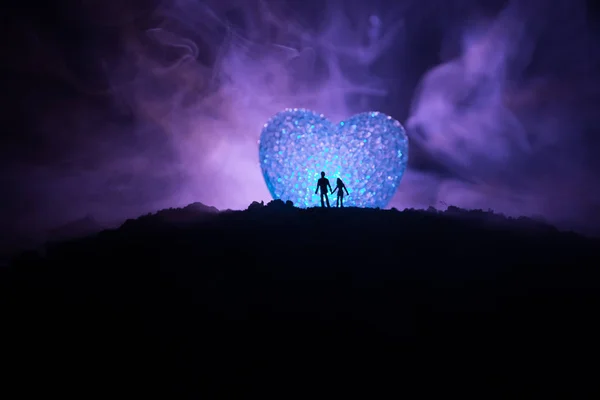 Silhouet van gelukkige paar staande achter grote gevormde hartsymbool op berg 's nachts. Groot hart zoals maan gloeien op mistige hemel. Aftelkalender voor Valentijnsdag decor foto — Stockfoto