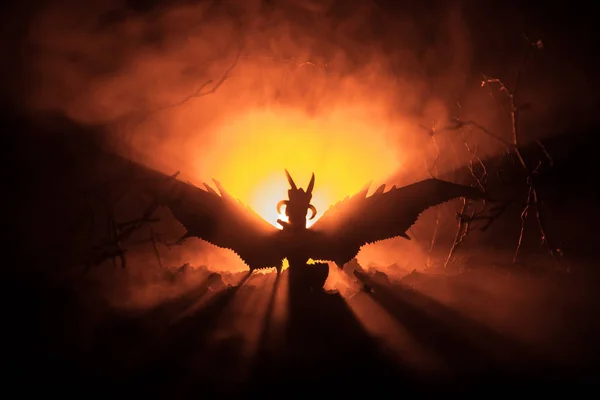 Silhouette de dragon respirant le feu avec de grandes ailes sur un fond orange foncé. Image d'horreur — Photo