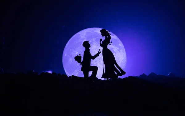 Geweldige scène van de liefde. Silhouetten van man vrouw of silhouetten van paar tegen grote maan bij achtergrond worden voorstel aangebracht — Stockfoto