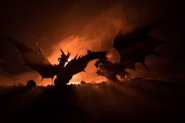 Silhouette of fire breathing dragon with big wings on a dark orange background clipart