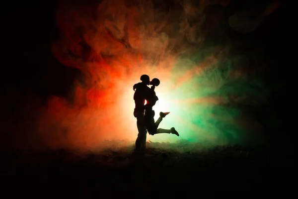 Love Valentine 's Day concept.Sillhouette of sweet young couple in love standing in the field and hugging on dark toned foggy background. Украшение с фигурками кукол на столе . — стоковое фото