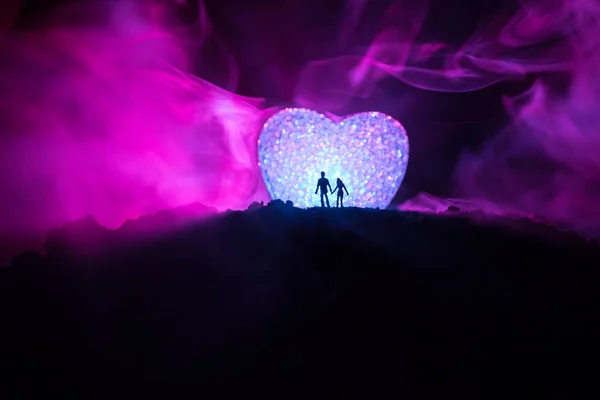 Silhouette of happy couple standing behind big shaped heart symbol on mountain at night. Big heart like moon glowing at foggy sky. Valentine`s day decor photo — Stock Photo, Image