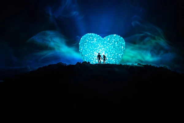 Silhouette of happy couple standing behind big shaped heart symbol on mountain at night. Big heart like moon glowing at foggy sky. Valentine`s day decor photo — Stock Photo, Image