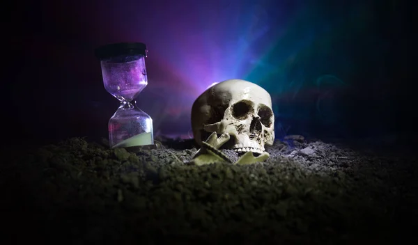 Cráneo y reloj de arena vintage sobre fondo nebuloso tonificado oscuro bajo haz de luz. Concepto de horror . —  Fotos de Stock