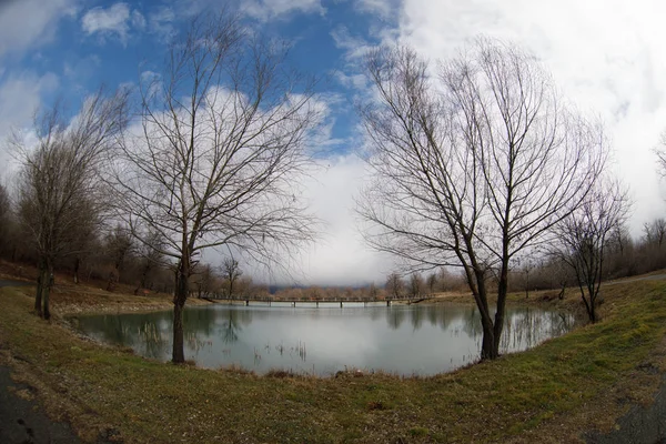 Waldsee mit Brücke während des sonnigen Tages mit Winterbäumen und blauem bewölkten Himmel. schöner natürlicher Bergsee mit Wald im Hintergrund und stürmischen Wolken am Himmel. — Stockfoto